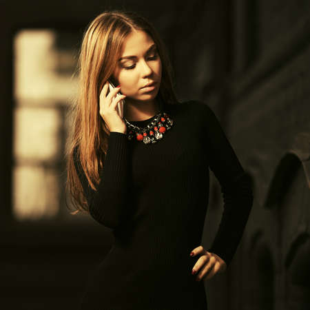 Young fashion woman calling on cell phone Stylish female model with long straight hair in black sweater dressの写真素材