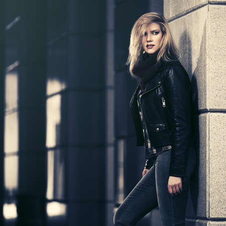 Young fashion blonde woman walking on city street  Stylish female model in black leather jacket and snood scarfの写真素材