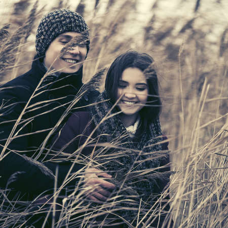Happy young fashion couple walking in thickets of bulrush Stylish man and woman in classic coats beanie and scarfの写真素材