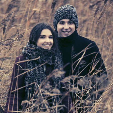 Happy young fashion couple walking in thickets of bulrush Stylish man and woman in classic coats beanie and scarfの写真素材