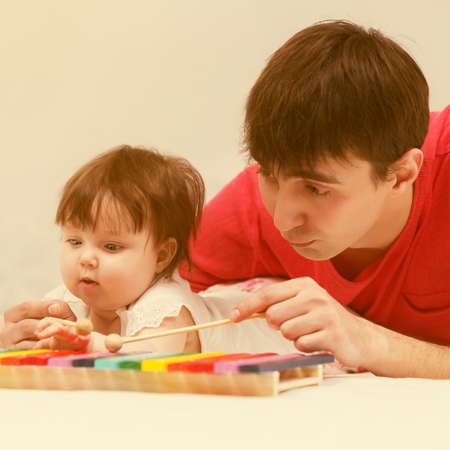 Father and baby girl playing xylophone toy on blanket at homeの写真素材