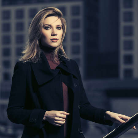 Young fashion blonde business woman walking on city street Stylish female model in classic black coat and brown sweaterの写真素材