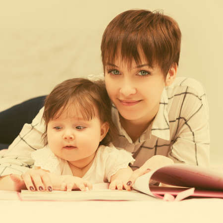 Happy young mother and little baby girl reading a book on bedの写真素材