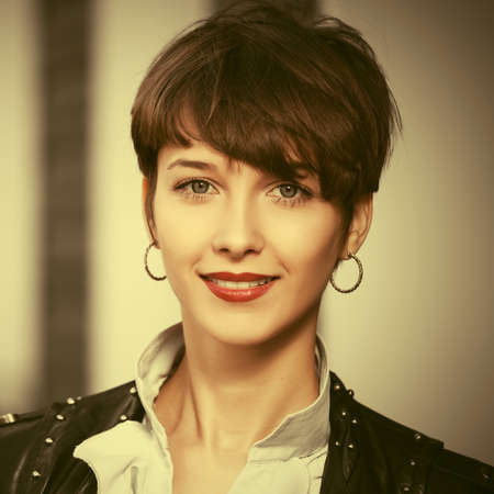 Happy young fashion woman walking on city street Stylish female model in black leather jacket with pixie hair styleの写真素材