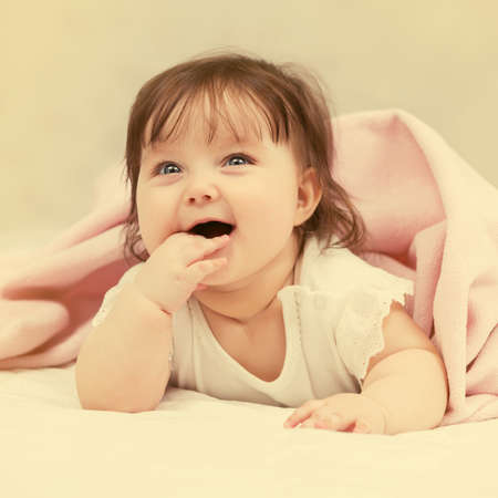 Happy six months old baby girl lying on blanket at homeの写真素材