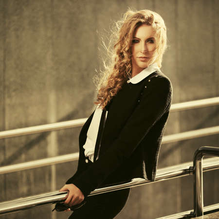 Young fashion blonde business woman leaning on railing Stylish female model in black jacket and white shirtの写真素材
