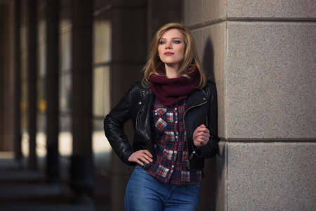 Young fashion blonde woman leaning on the wall  Stylish female model in black leather jacket and snood scarfの写真素材