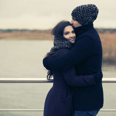 Happy young fashion couple in love embracing outdoor Stylish man and woman in classic coats beanie and scarfの写真素材