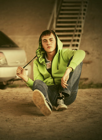 Sad teen boy in depression sitting on the ground Stylish trendy male model in light green hoodie and...