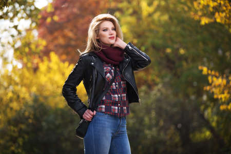 Young fashion blonde woman walking in city park  Stylish female model in black leather jacket and snood scarfの写真素材
