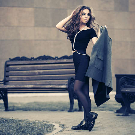 Young fashion woman with long curly hairs with gray sleeveless coat Stylish female model in black crop top and skirtの写真素材
