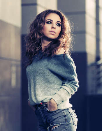 Happy young woman with long curly hairs walking on city street Stylish fashion model in blue pullover and ripped jeansの写真素材
