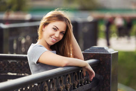 Happy young woman leaning on railing Stylish fashion model with long straight hair in gray t-shirtの写真素材
