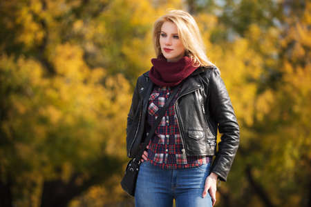 Young fashion blonde woman walking in city park  Stylish female model in black leather jacket and snood scarfの写真素材