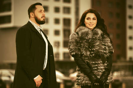 Happy young fashion couple walking on city street  Stylish trendy man in classic black coat and woman in fox fur jacketの写真素材