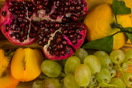 Fruit ripe red pomegranate, white grapes, orange mandarin with green leaves and persimmonの写真素材