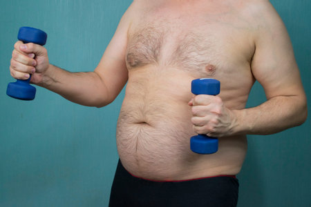 fat man with a belly and a naked torso doing sports with dumbbells for weight loss