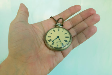 old round pocket mechanical watch in hand on palm on blue background