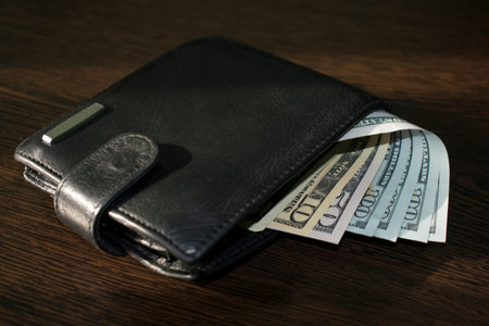 leather black purse with American dollars on a brown wooden table