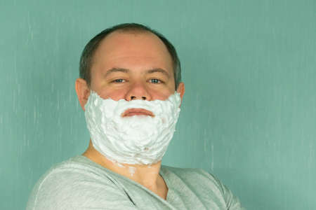 A man in shaving foam on his face is about to shave, on a green backgroundの写真素材