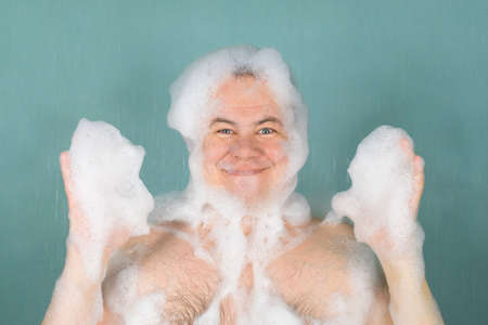 A man smiles in a soapy foam on his head and raised his hands washed on a green backgroundの写真素材