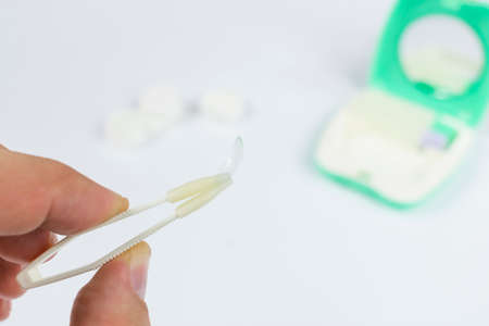 hand holding tweezers with a transparent silicone eye contact lens on a white background with a lens storage container with a mirror out of focusの写真素材