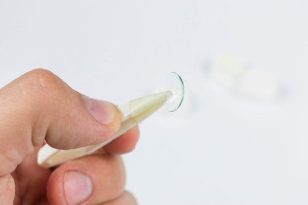 hand holding tweezers with a transparent silicone eye contact lens on a white background with a lens...