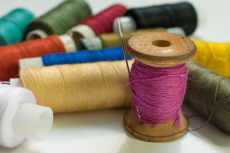 red, white, yellow, black, brown thread with a wooden bobbin and inserted needle for sewing,...