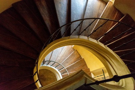 Round brown wooden staircase with iron railings, descending downwards