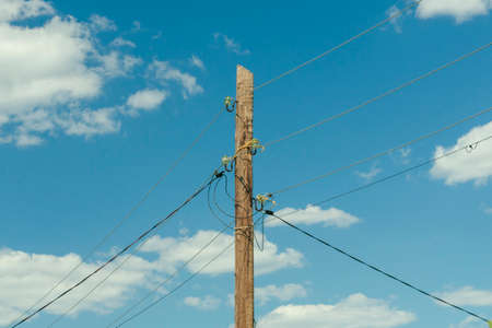 old wooden power pole entangled wires with electricity, against a blue sky backgroundの写真素材