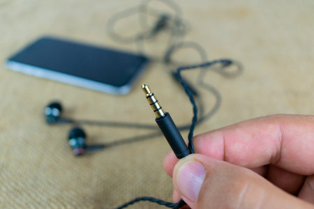 a plug of wire headphones in the hand, on the background of the smartphone and the earphones...