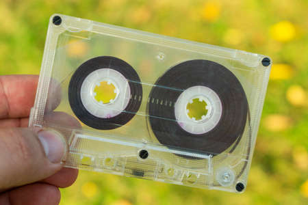 analogue old audio cassette in hand on a yellow-green grass background in autumn, close-upの写真素材