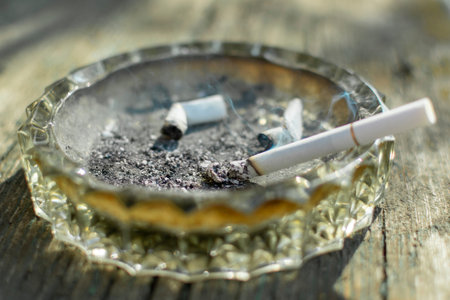 smoking cigarette in a glass ashtray with cigarette butts
