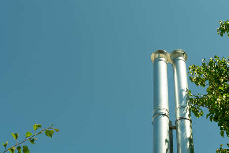 two shiny stainless steel chimney pipes for ventilation and emission of combustion products, carbon dioxide against a blue skyの写真素材