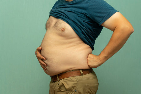 close up portrait of overweight obese mans hand holding his big belly
