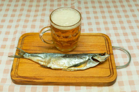 salty dried smelt fish, as a snack and a glass mug of light beer on a wooden kitchen boardの写真素材