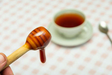 wooden spoon with dark mustard honey and a cup of hot tea in unfocused in the backgroundの写真素材