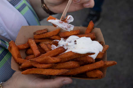 Young woman holds a bowl of sweet potato fries with mayo in front of her bodyの写真素材