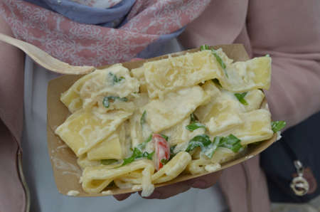young woman eats tagliatelle with cheese cream sauce in cardboard bowlの写真素材