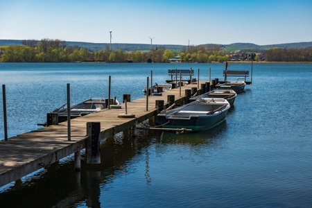 wooden jetty with rowing boats in a blue lakeの写真素材