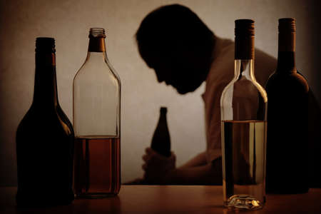 silhouette of a person drinking behind bottles of alcohol with added filter silhouette of a person drinking behind bottles of alcohol with added filter