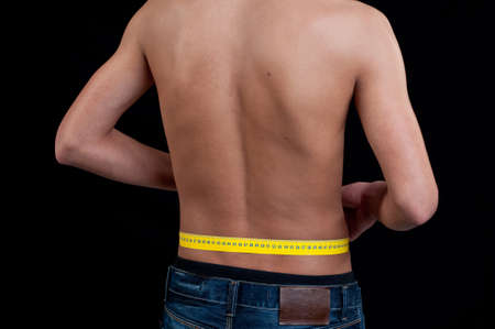 A young man who measure their waist rear view on black backgroundの写真素材