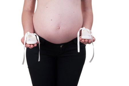 Pregnant woman holding pair of white shoes for baby