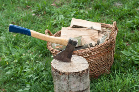 An axe stuck in a log in front of basket with logs fireの写真素材