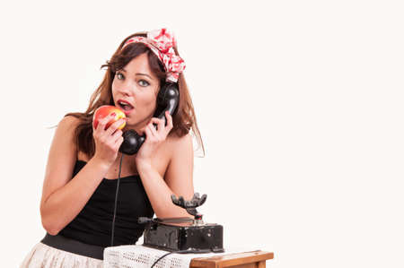 Fashion young woman with a retro look speaks at a vintage phone while she bite from a red appleの写真素材