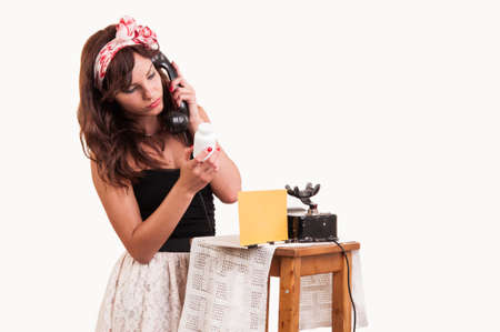 Fashion young woman with a retro look speaks at a vintage phone and reads from a bottle with medicineの写真素材