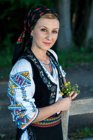 beautiful singer with flowers in her hands posing at countryside, romanian folkloreの写真素材