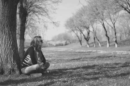 thoughtful brunette sitting under a tree in a park (Black-and-white photo with high contrast)の写真素材