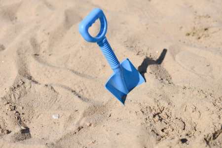 blue beach shovel stuck in the sand by a childの写真素材