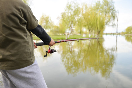 Closeup of fisherman`s hand holding rod with spinning. Fishing reel visible. Selective focus